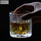 Hammered crystal rocks glass with amber drink, hand adjusting the rim.