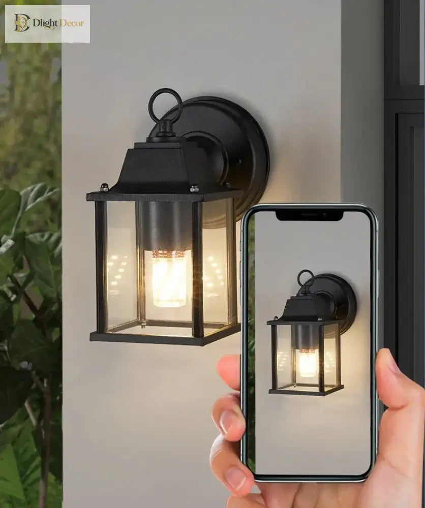 Black exterior wall lamp with clear glass lantern and warm light, shown with smartphone