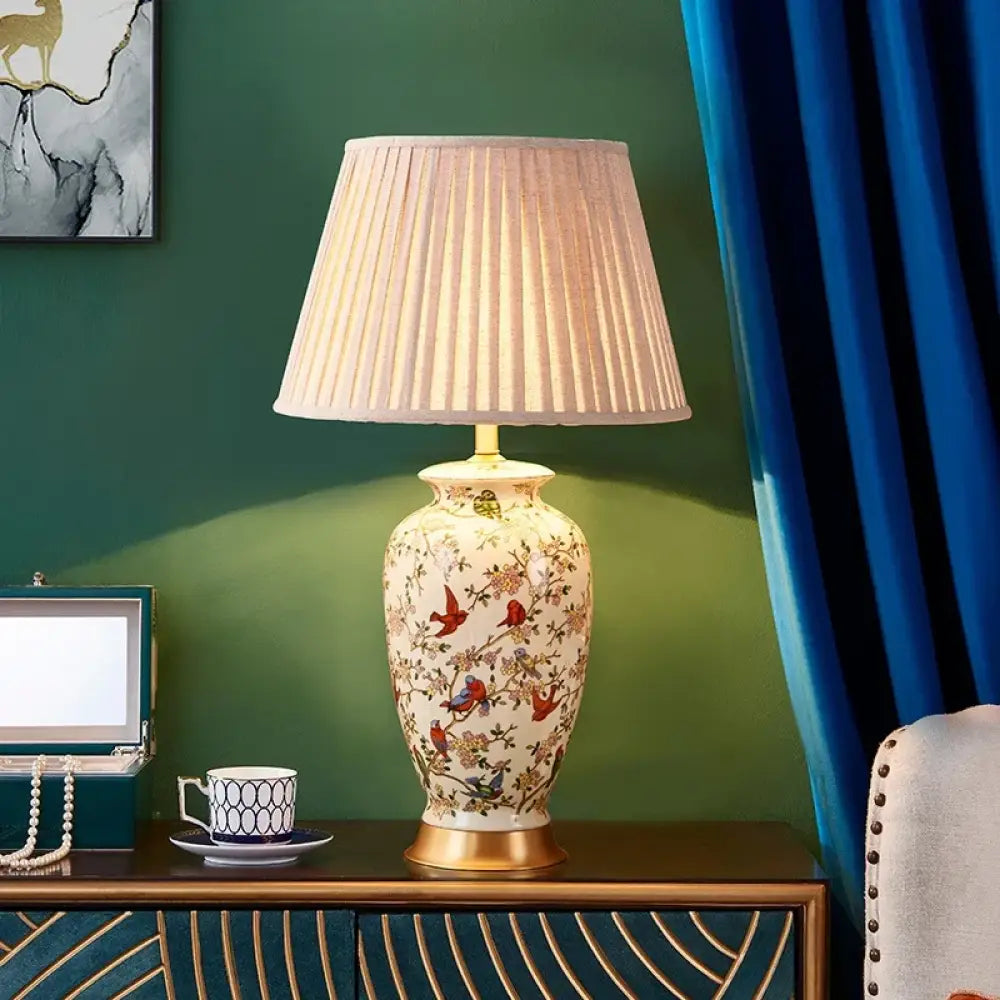 Floral ceramic table lamp with pleated white shade and brass base, warm lit glow