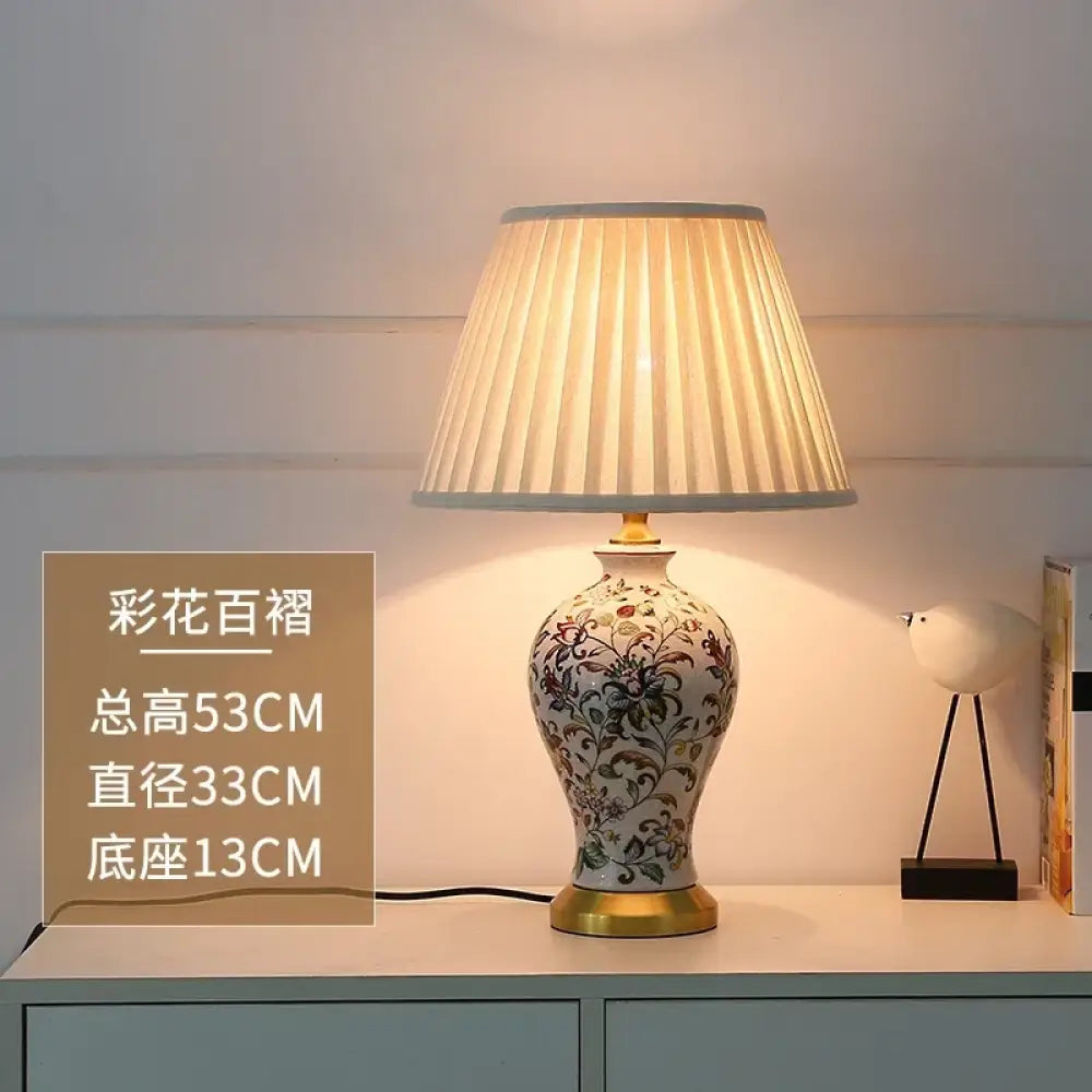 Floral ceramic table lamp with large pleated shade and gold base on console.