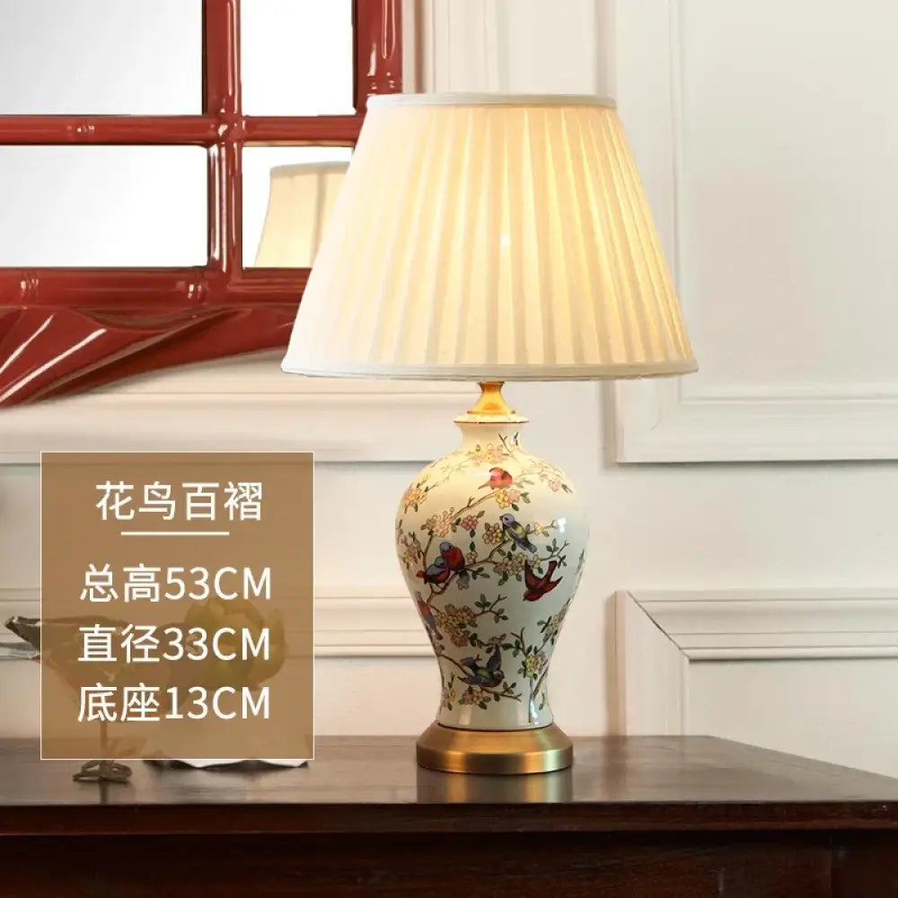Floral ceramic table lamp with pleated white shade and gold base on wooden surface.