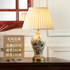 Floral ceramic table lamp with pleated white shade and gold base on wooden surface.