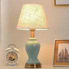 Glazed ceramic table lamp with gold base and beige fabric shade, close-up.
