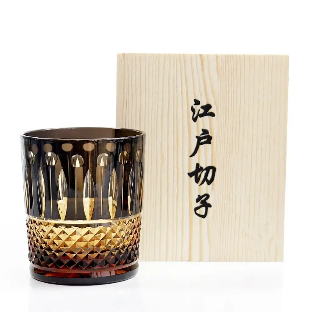 Diamond-cut crystal whiskey glass next to a light wood gift box with printed characters