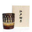 Diamond-cut crystal whiskey glass next to a light wood gift box with printed characters
