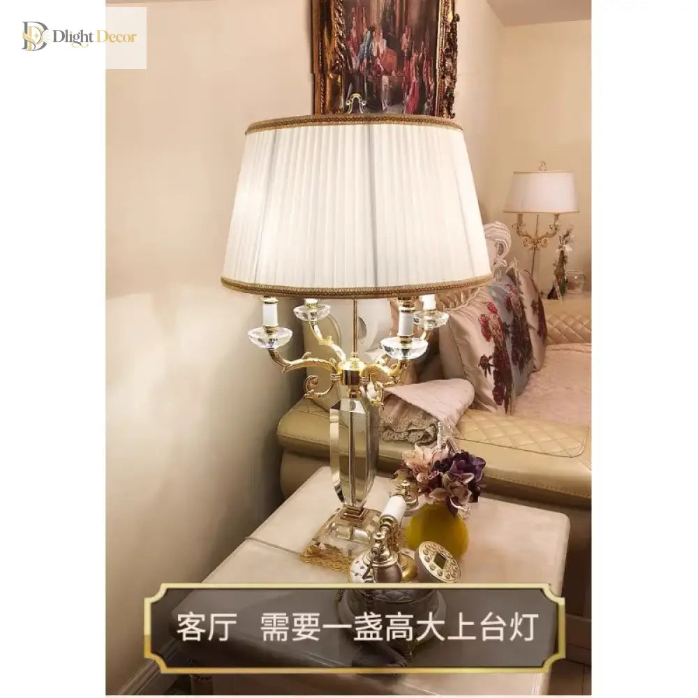 Gold crystal table lamp with pleated white shade and twin-branch candelabra arms.