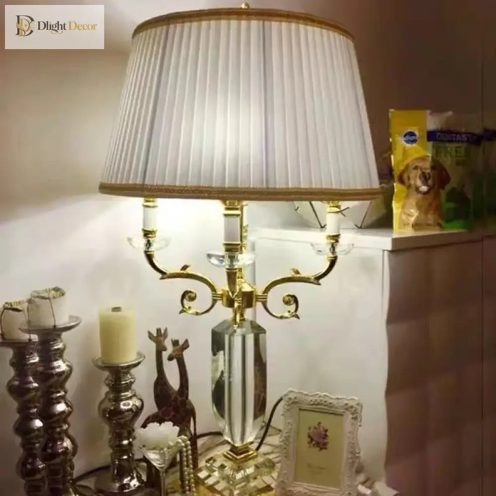 Gold crystal table lamp with pleated white shade and decorative scroll candelabra base.