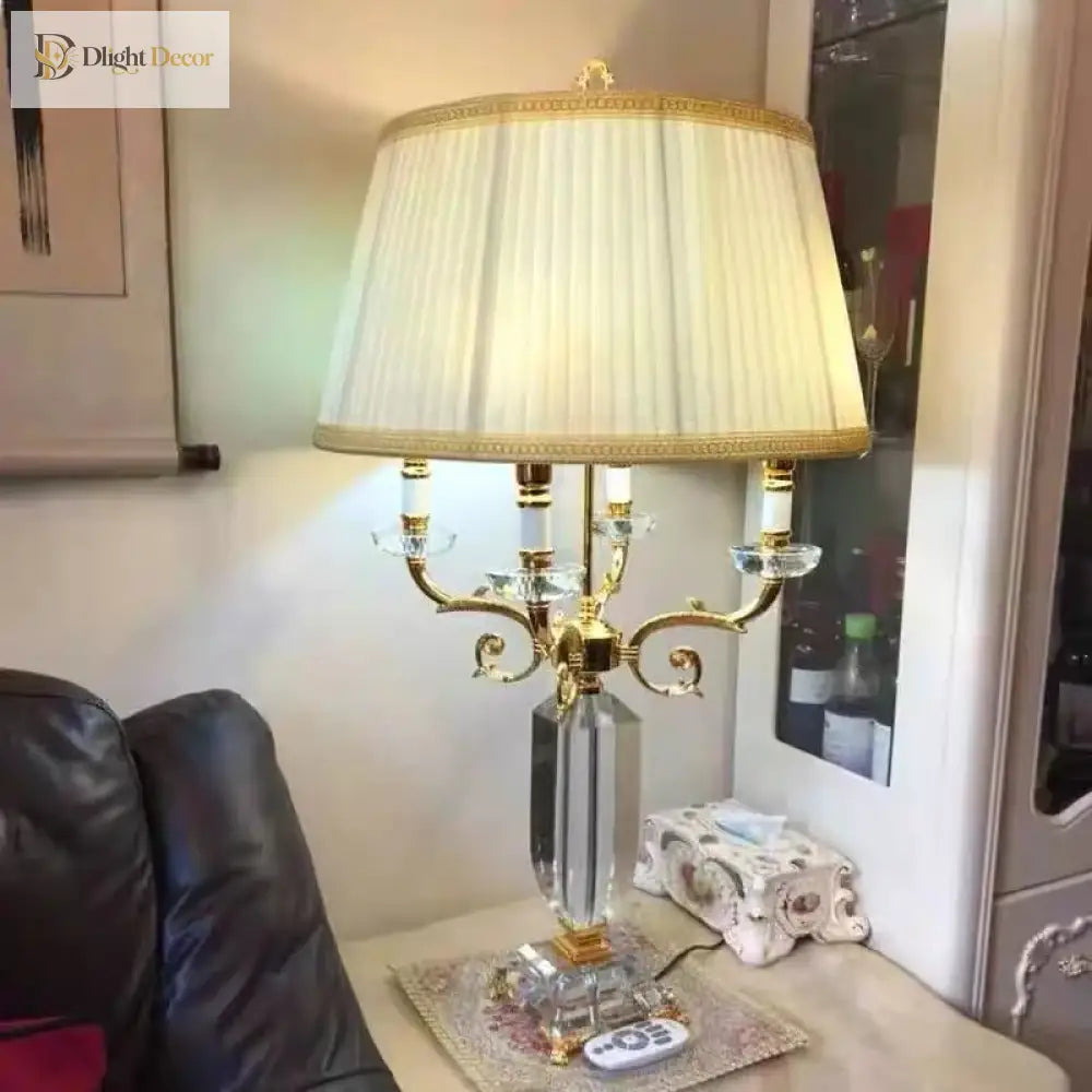 Gold and clear crystal table lamp with pleated white shade, curved arms, and crystal column.