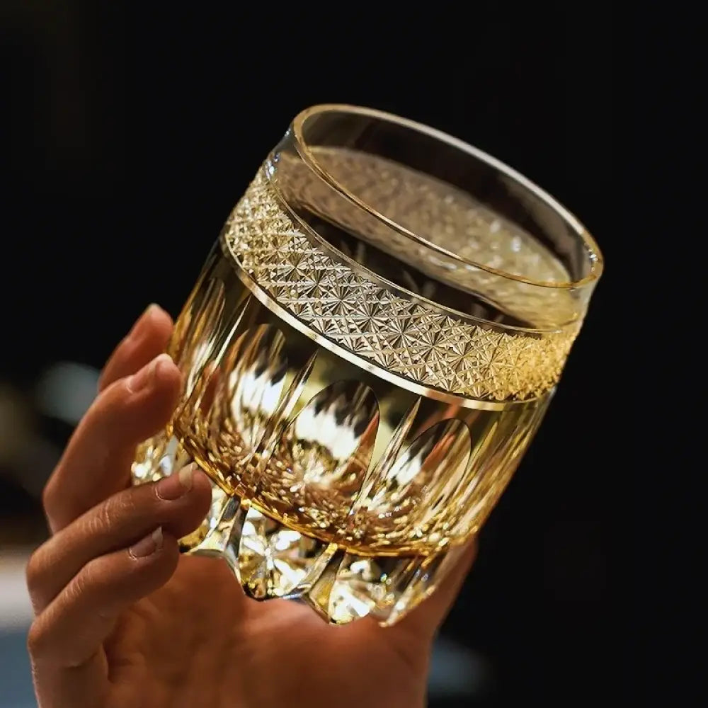Amber cut crystal whiskey tumbler, hand-held view, faceted base and patterned band